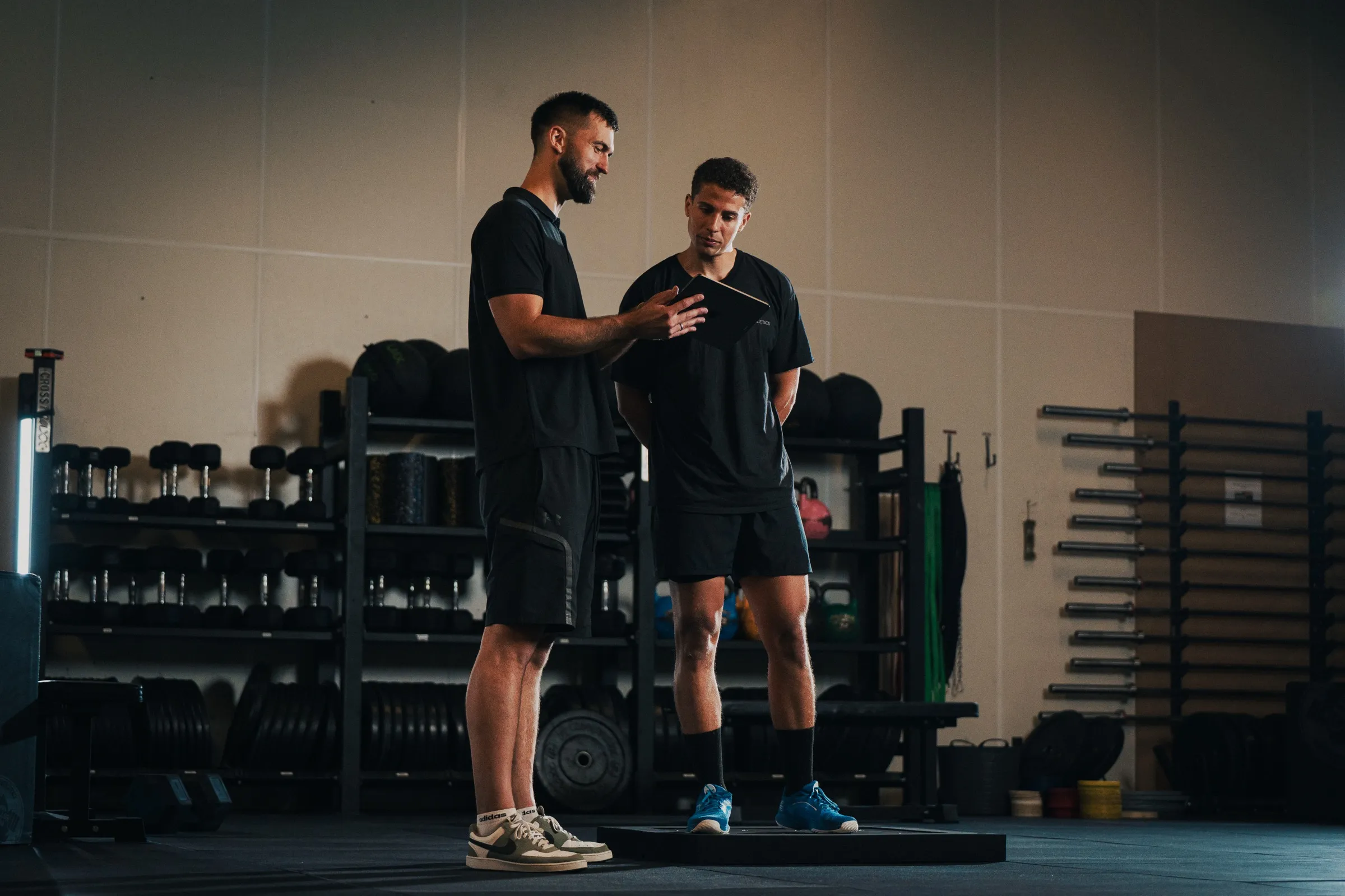 A coach briefing an athlete standing on PlateMate force plates, going through the test on a tablet.