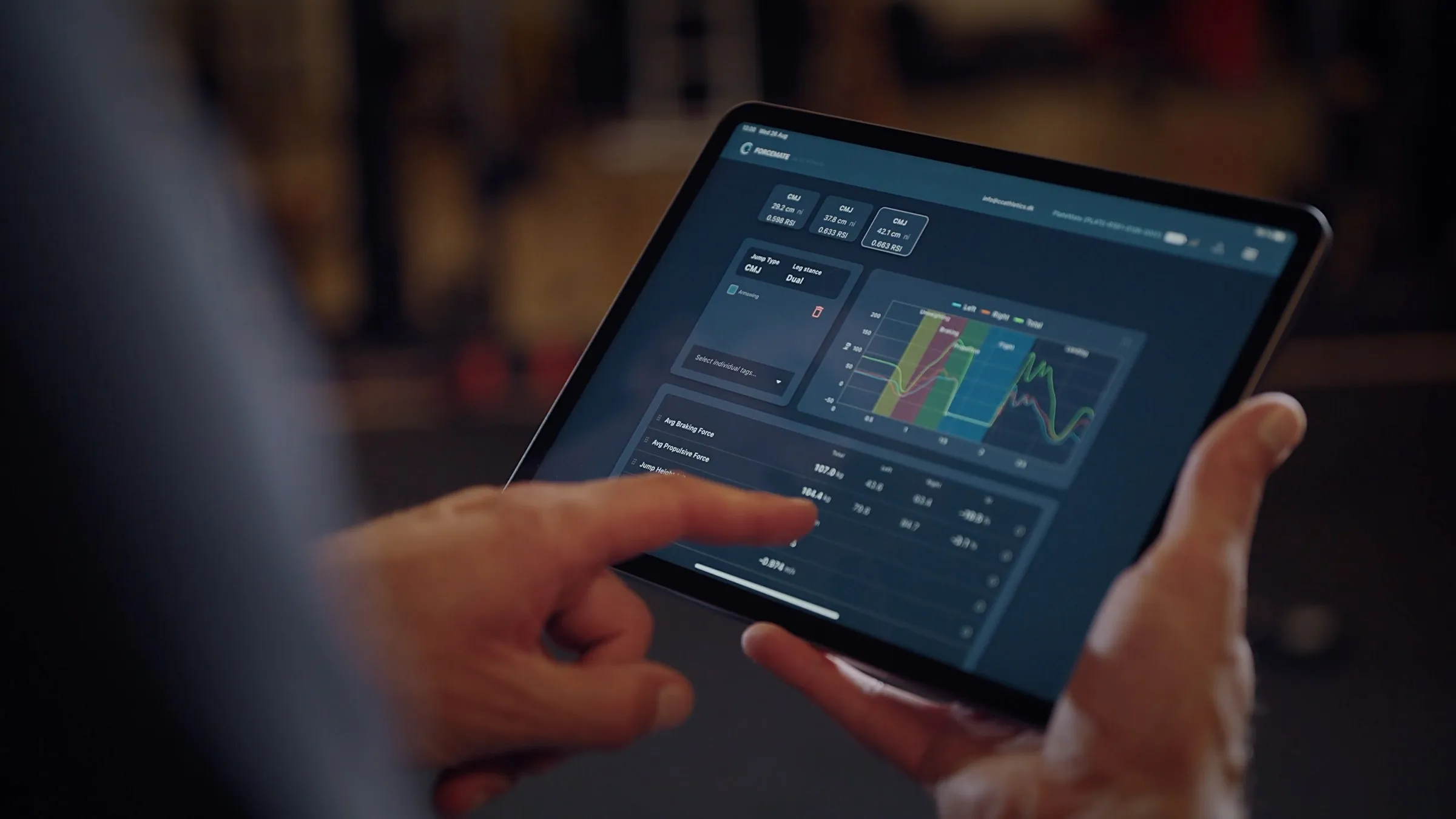 A tablet held in both hands showing the ForceMate results screen — countermovement jump height, RSI and a left/right force curve.