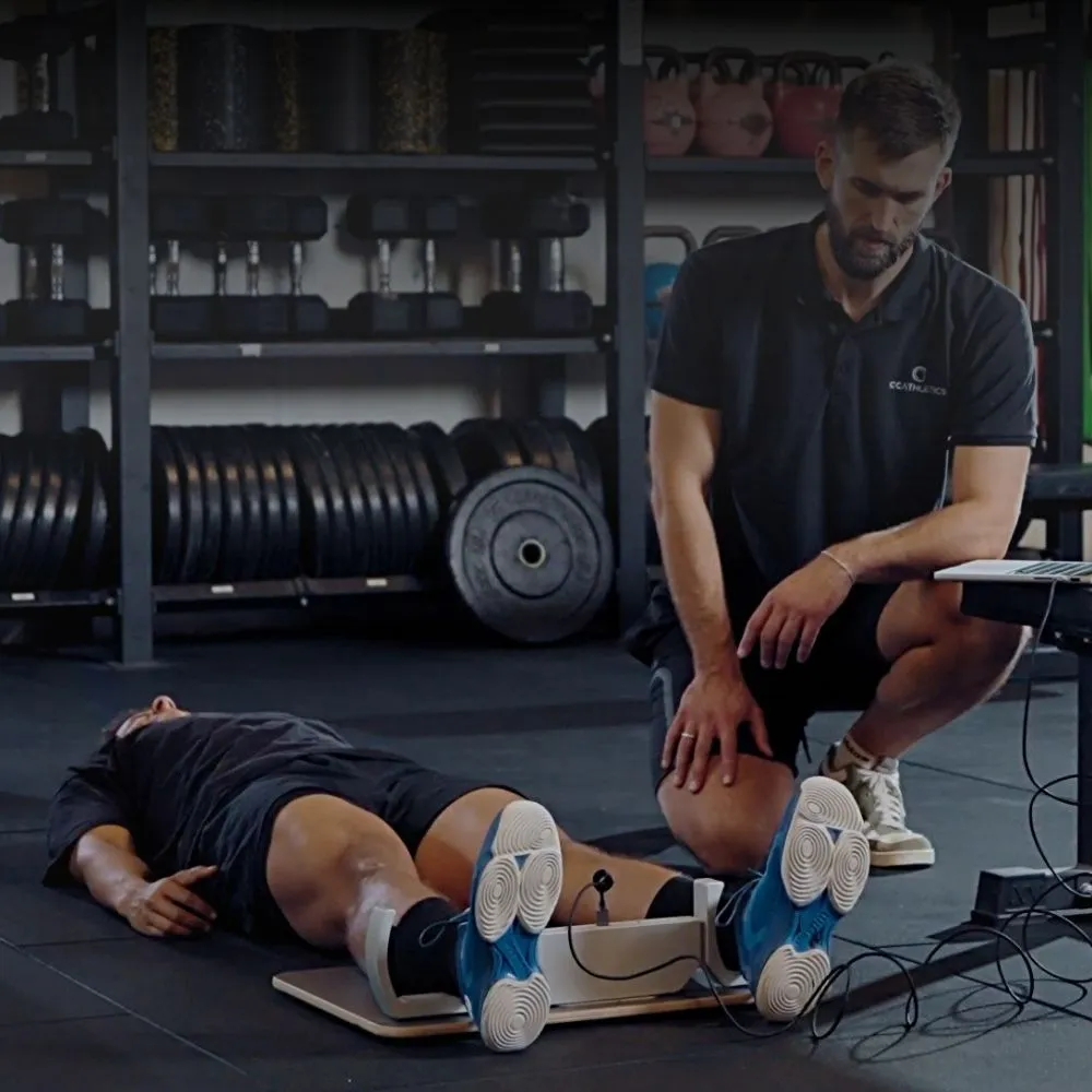 A coach carrying out a GroinMate adductor squeeze test on an athlete lying on the gym floor